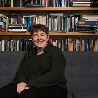 A person sits on a sofa in front of a bookshelf