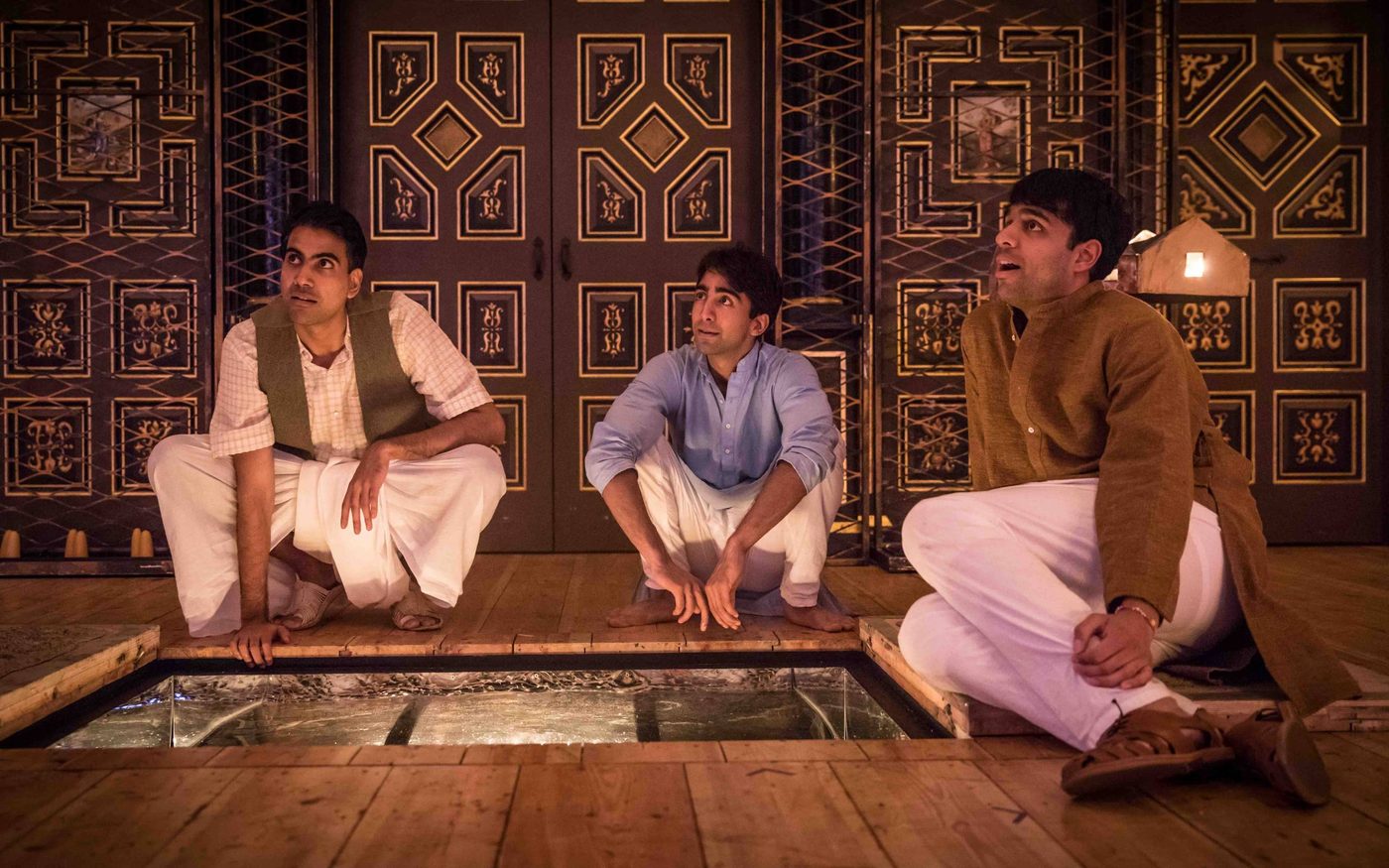 Three actors sit around a trap door on a candelit stage.