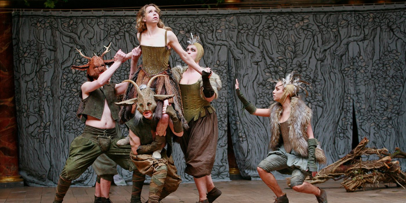 A woman wearing a green corset dress is lifted into the air by a group of people wearing fur and antlers.
