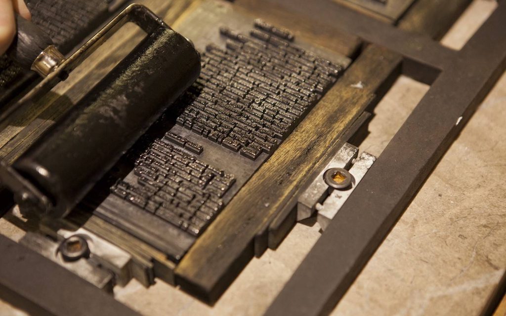 A close-up of ink being rolled onto letters on a printing press