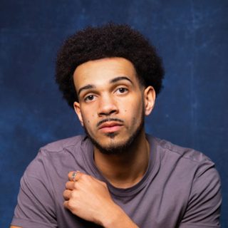Headshot of Simeon Desvignes looking directly at the camera in front of a blue background.