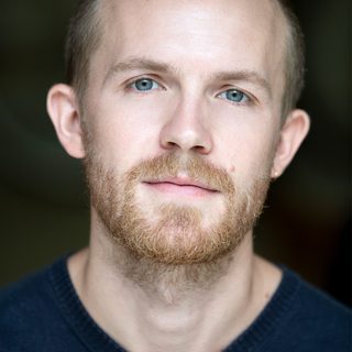 An actor with a short beard looks to the camera